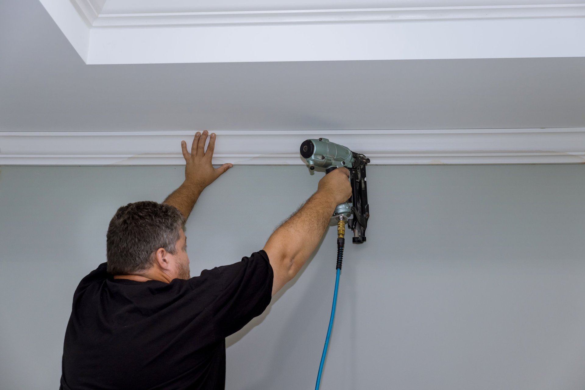 Carpenter fitting crown molding between wall and ceiling in a finely finished interior