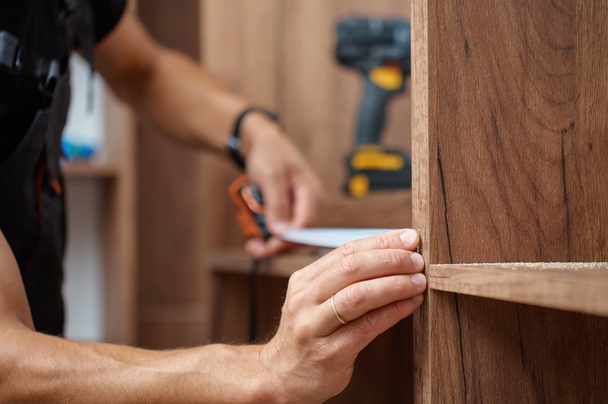 A craftsperson measuring and marking a wooden board at a workbench.