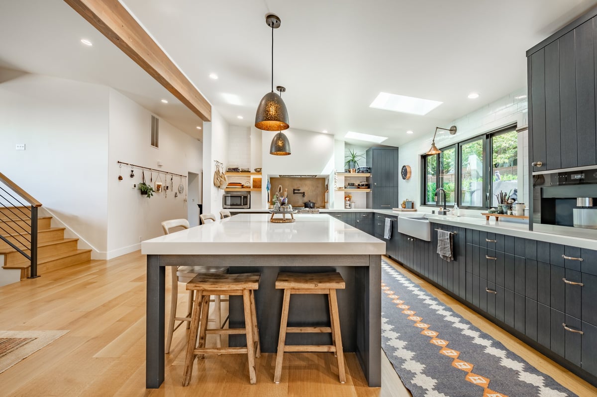 Modern restored kitchen with dark cabinetry, white countertops, and warm wood flooring after complete renovation