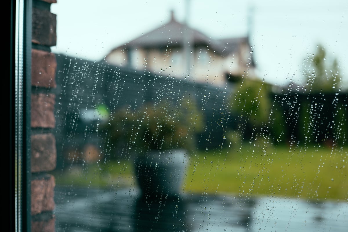 Raindrops on a window with a house visible beyond the glass.