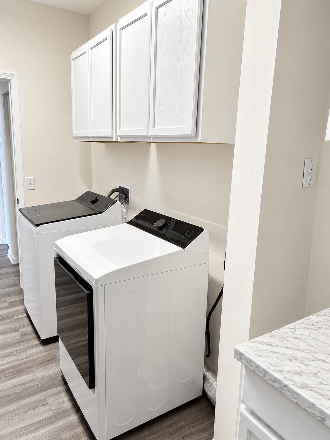 White Samsung washer and dryer with dark control panels beneath white upper cabinets in Arlene H.’s renovated laundry room.