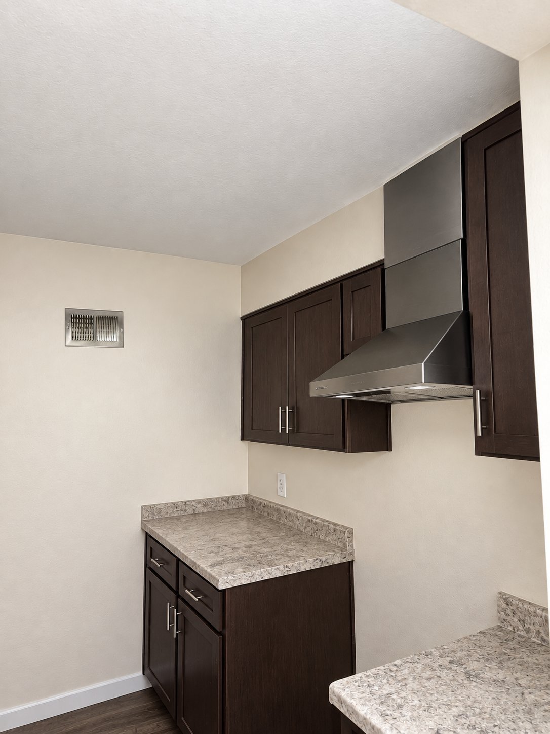 Modern kitchen with dark cabinets, granite countertop, stainless steel range hood, and cream-colored walls