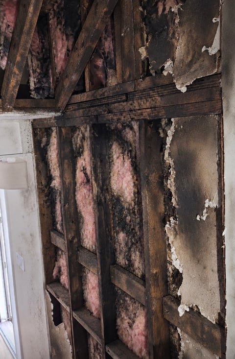Interior wall with severe fire damage, charred wooden framing, peeling paint, and soot stains from floor to ceiling