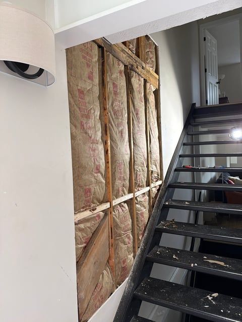 Stairwell with floral patterned fabric panels hung on white wall and black metal staircase