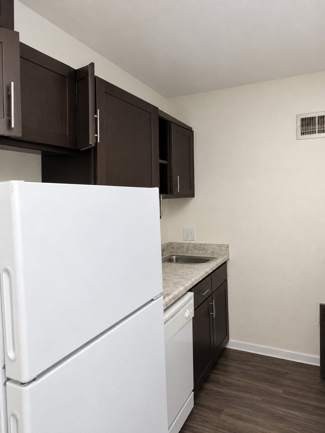 Modern kitchen with white refrigerator, dark brown cabinets, granite countertop, and dark hardwood flooring