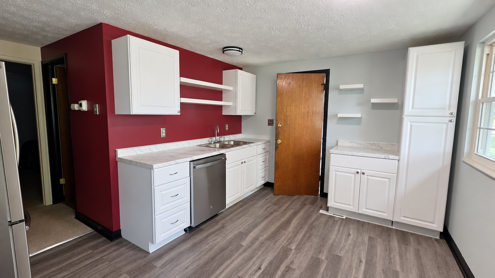 Kitchen renovation for Janet M. in Reynoldsburg, Ohio, featuring white cabinetry, a burgundy accent wall, floating shelves, and gray wood-look flooring.