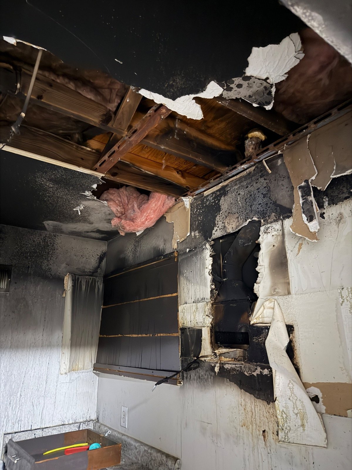 Fire-damaged ceiling and walls showing charred drywall, exposed wood beams, and structural damage in an interior room