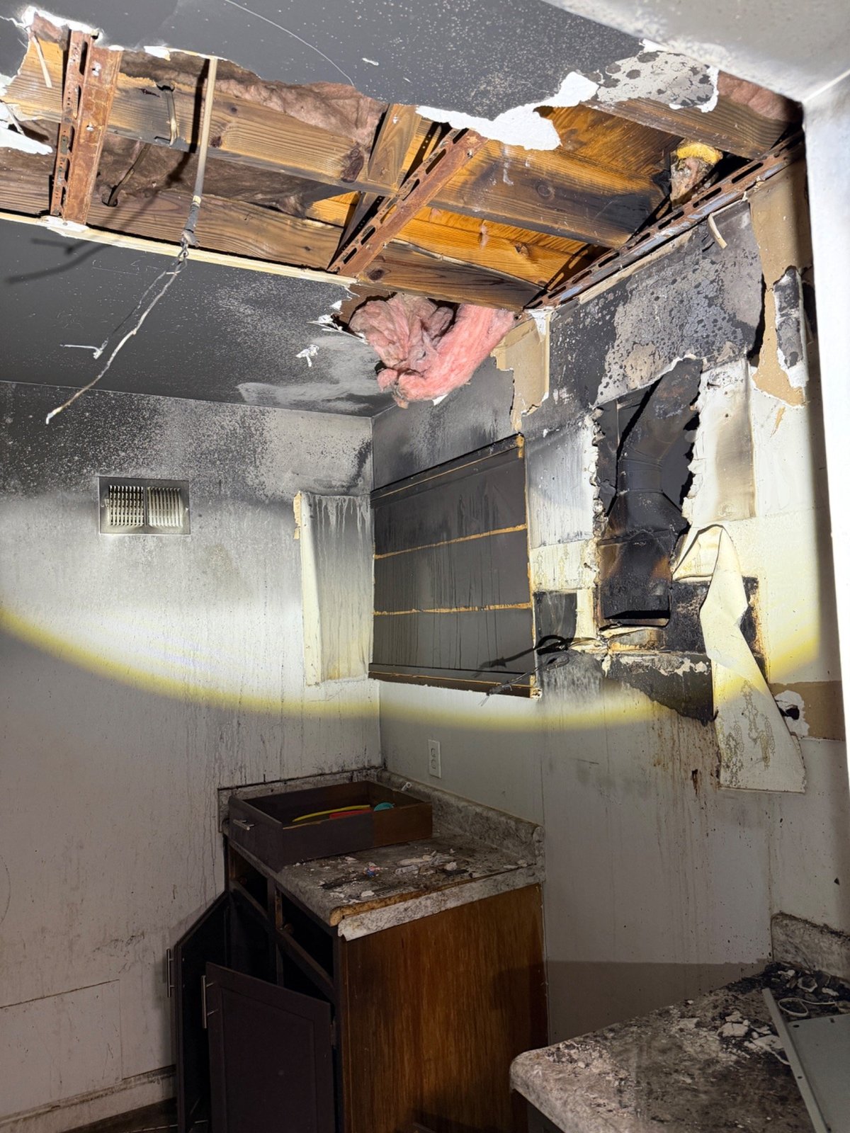 Fire-damaged bathroom interior with charred ceiling, exposed wooden beams, burned walls, and debris-covered fixtures