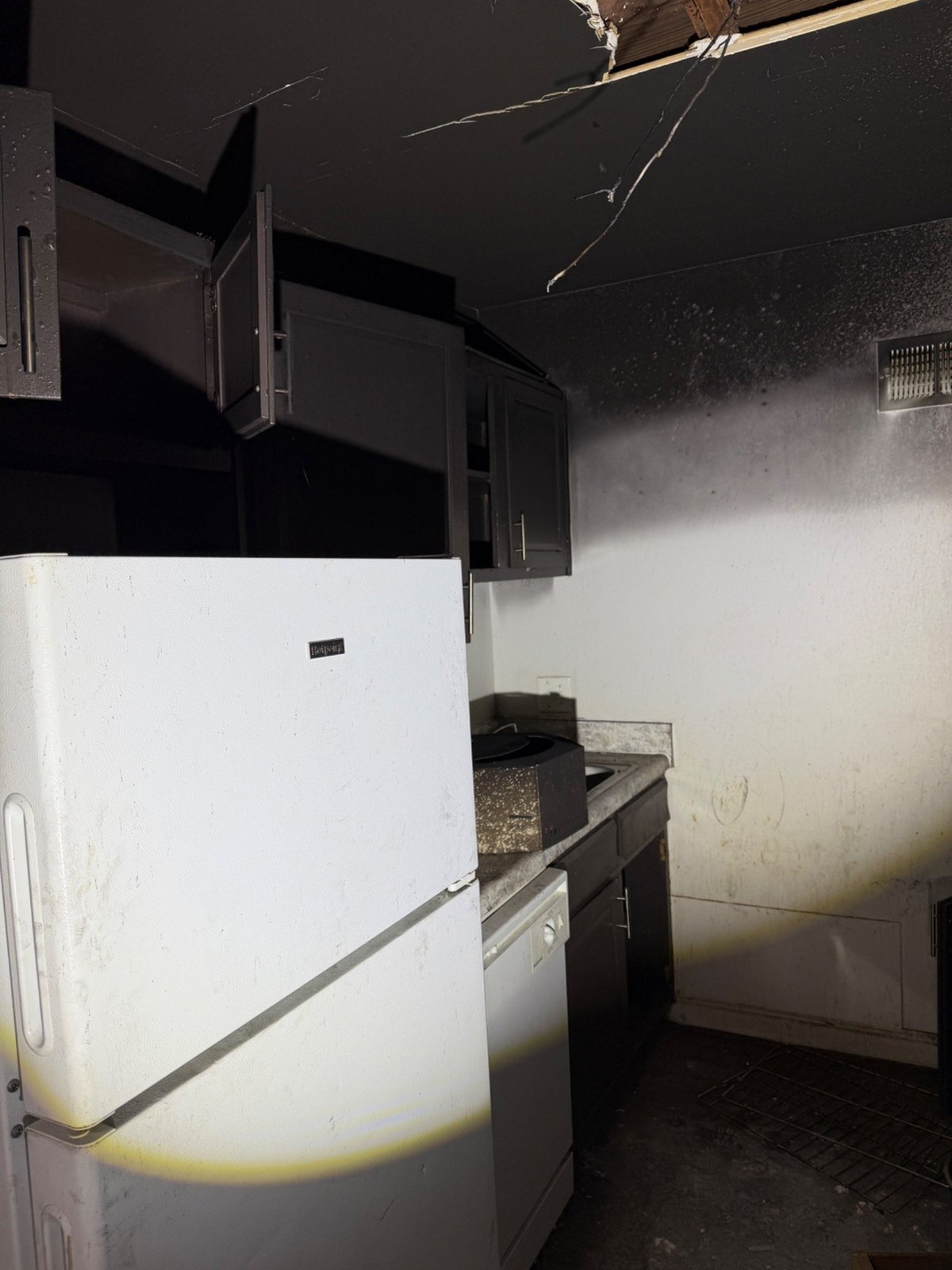 Damaged kitchen with a white refrigerator, black stove, and burnt ceiling showing signs of fire damage