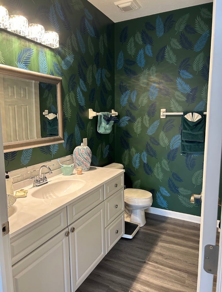 Primary bathroom renovation for Arlene H., featuring green walls with blue and green botanical detailing and a long white vanity.