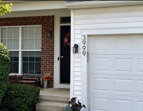 Front entrance of a brick house with white garage door, address 3976, black front door, and window planter with flowers