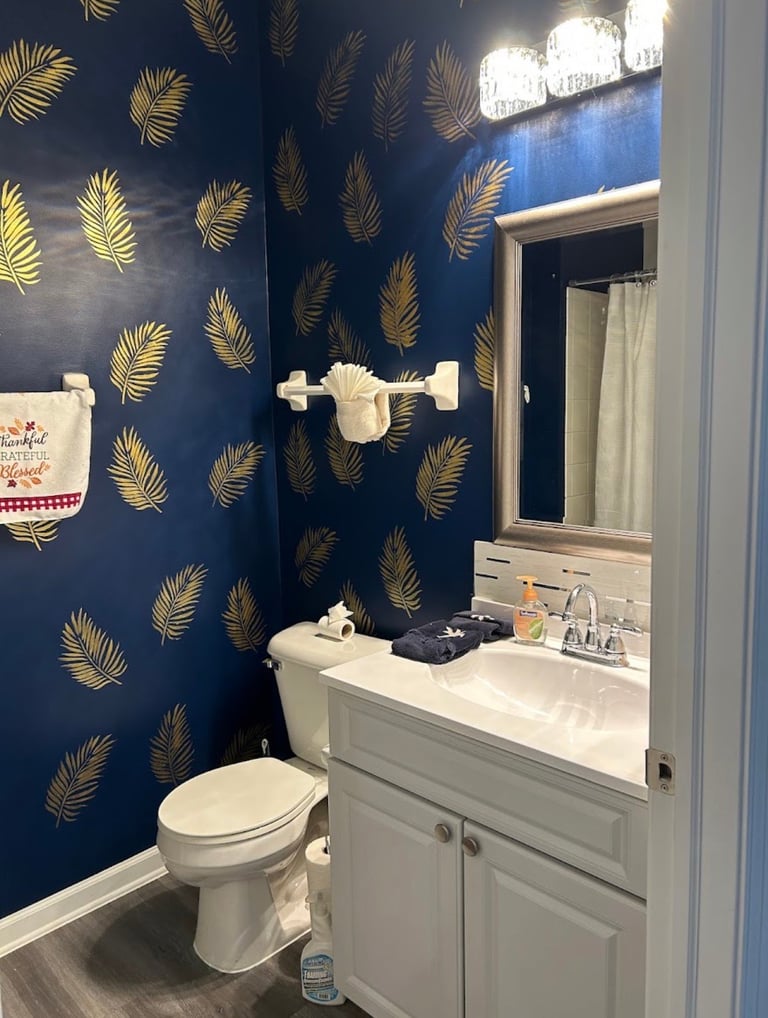 Guest bathroom renovation for Arlene H., featuring blue walls with gold botanical detailing and a white vanity.