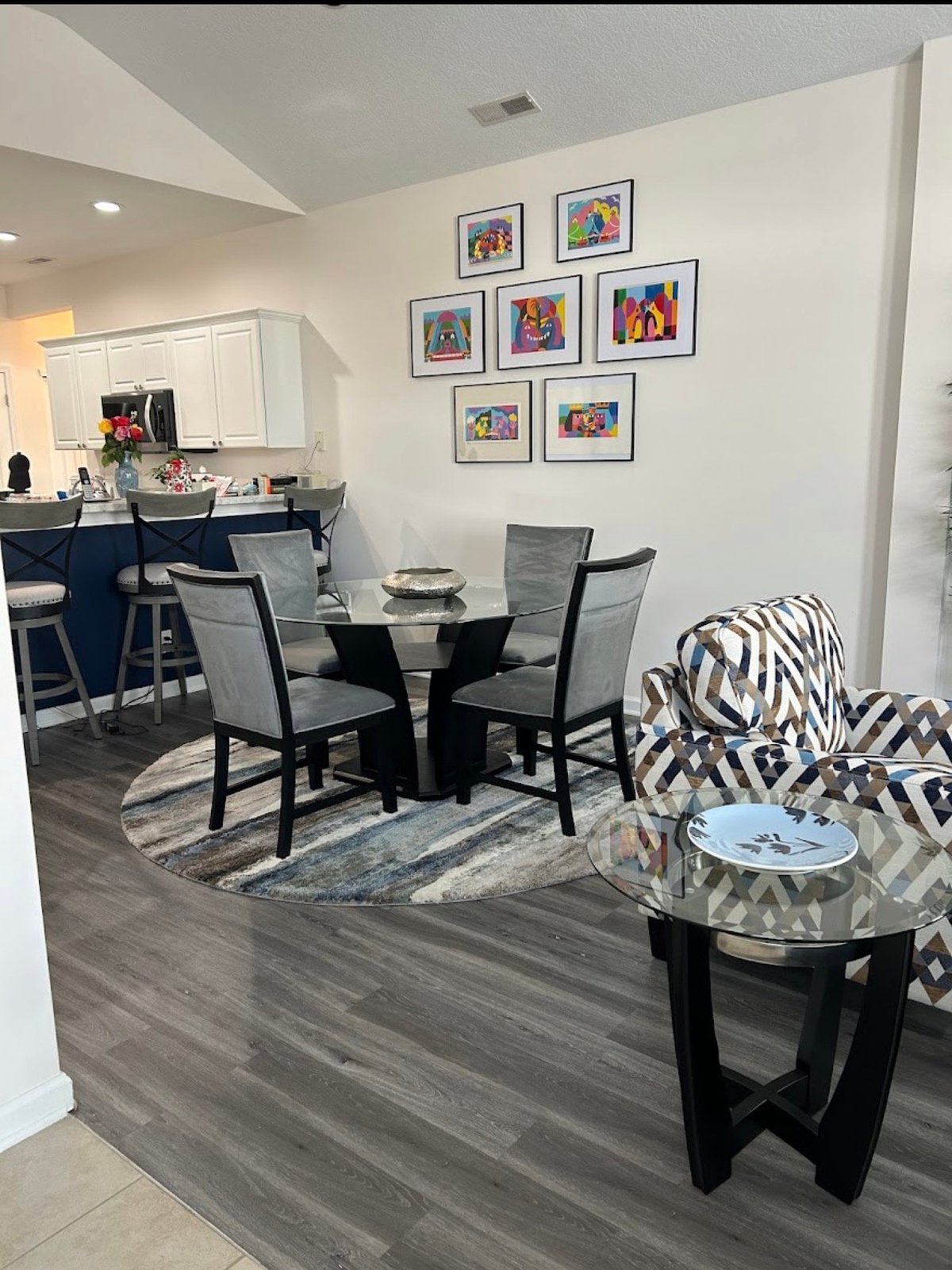 Renovated dining room and kitchen for Arlene H., featuring a glass dining table, white kitchen cabinets, and gray wood-look flooring.