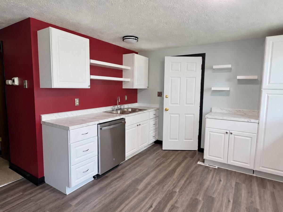 Modern kitchen with white cabinets, stainless steel appliances, red accent wall, and wood-look flooring