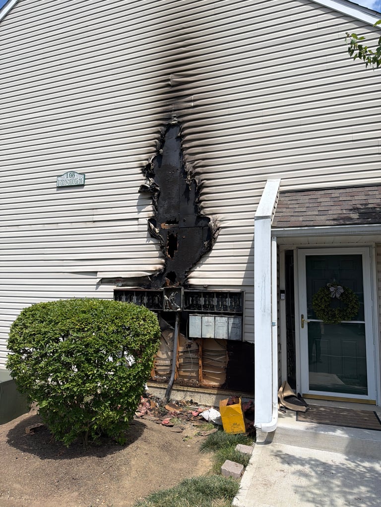 Fire-damaged siding on white house with burned vertical strip, green shrub and door entry visible